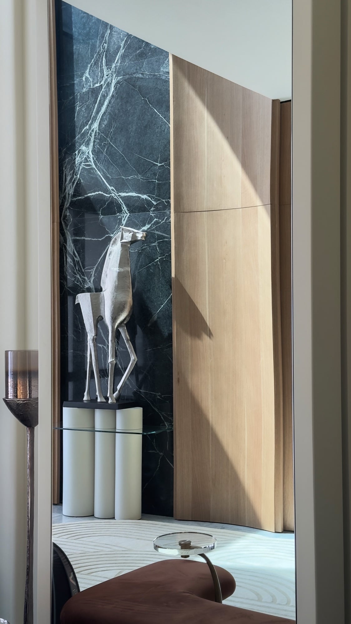 A silver deer sculpture on a fluted plinth against a dark green marble panel, framed by a pale timber door, designed by Radwa Interiors.