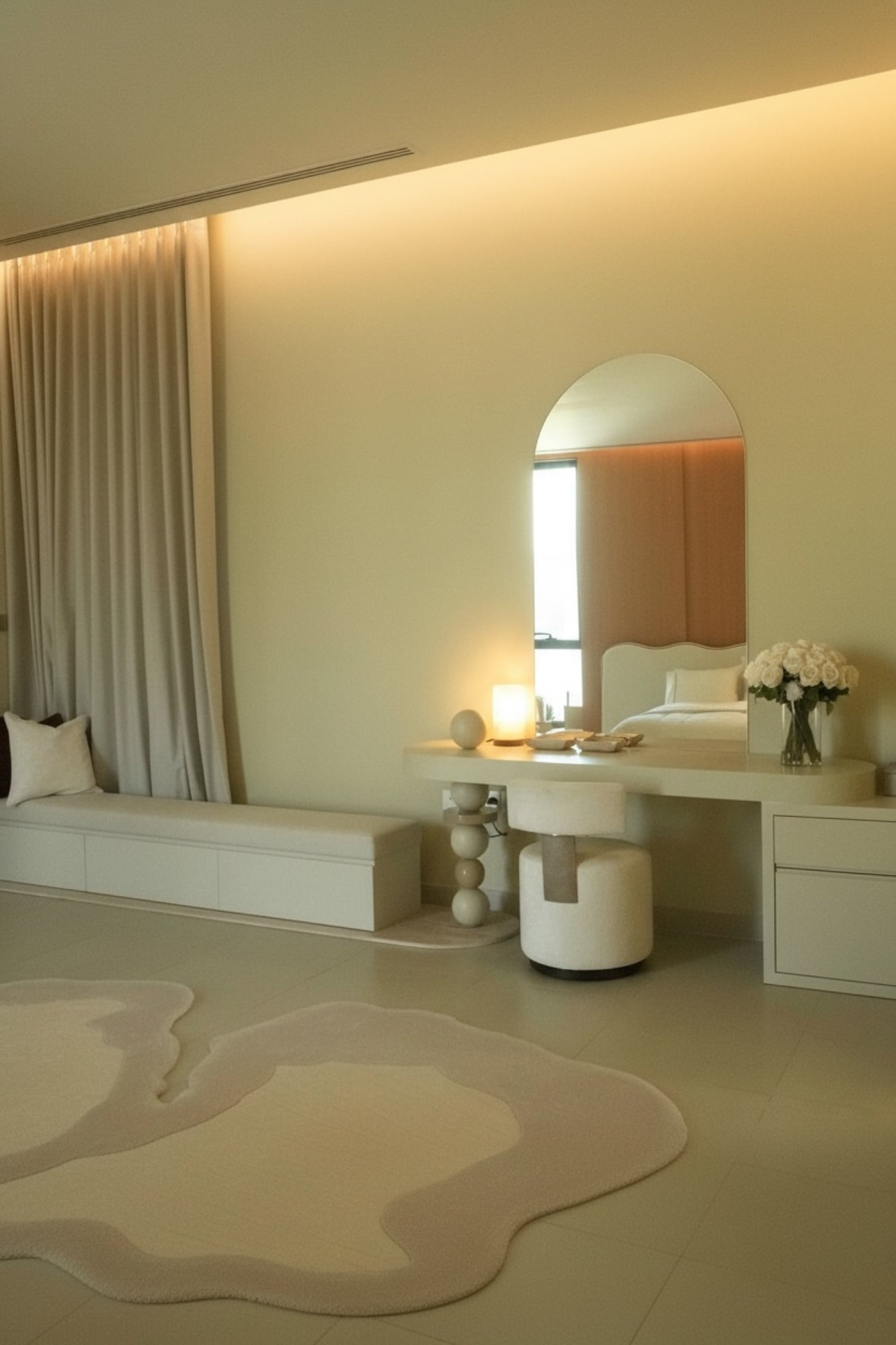 A bedroom dressing area with an arched mirror over a built-in vanity, a boucle stool and a soft cream rug, designed by Radwa Interiors.