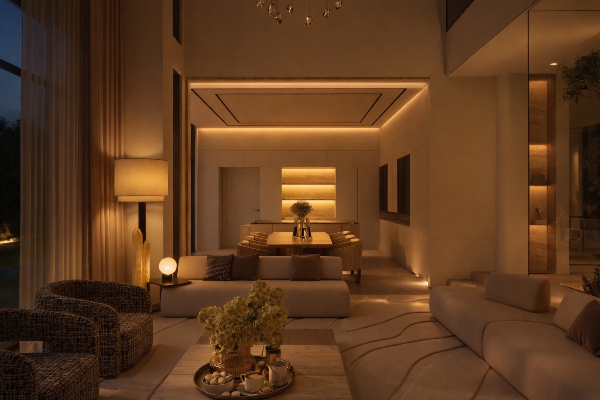 A living room at dusk, warmly lit, with woven armchairs and a low sofa before a dining table under a recessed light trough, designed by Radwa Interiors.