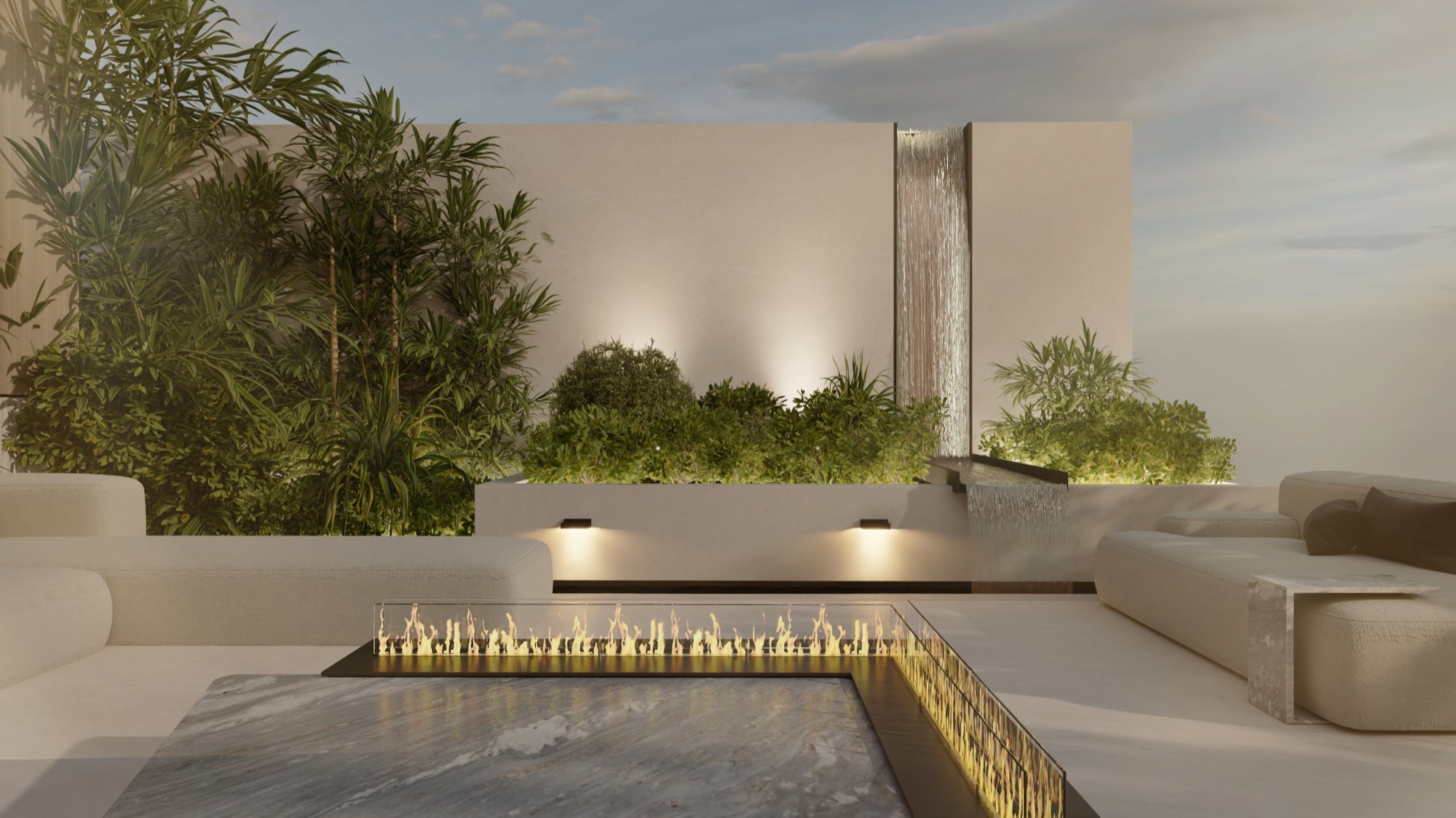 A terrace at dusk with a linear fire table and a water blade on a rendered wall, framed by dense planting, designed by Radwa Interiors.