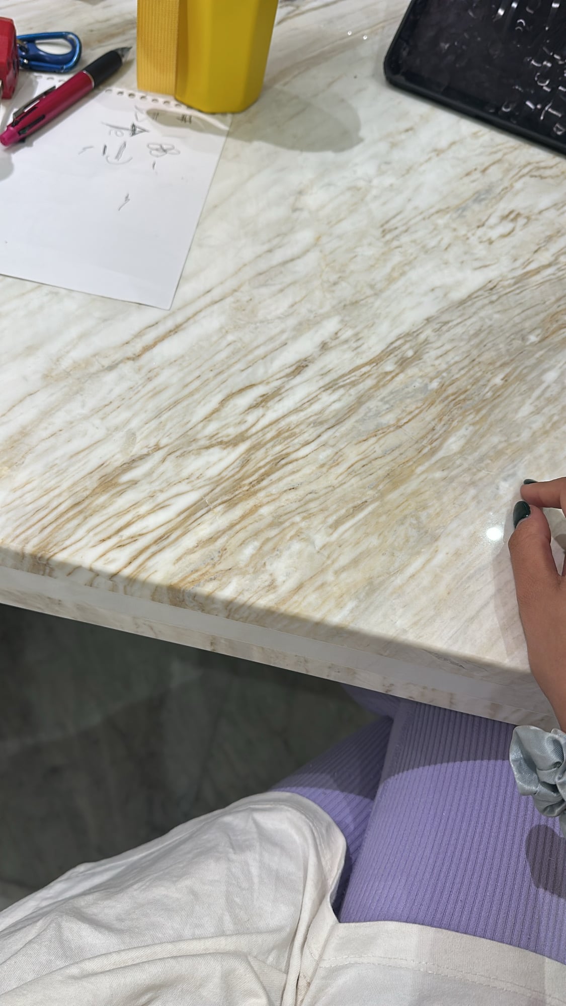 A hand marking out a veined marble slab on a workbench, with tools and a drawing alongside, designed by Radwa Interiors.