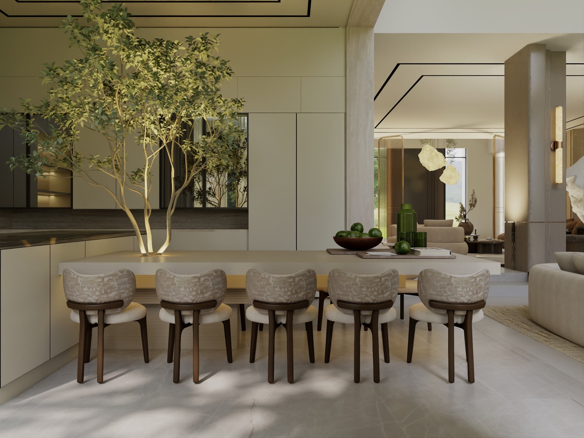 A kitchen island with five upholstered chairs and a bowl of limes, beside a slender tree lit from below, designed by Radwa Interiors.